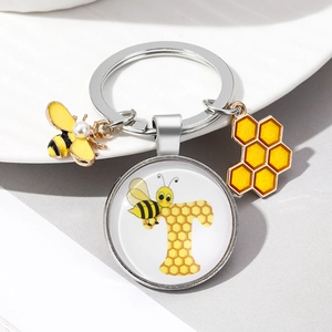 Detail of bee keychain with letter T pendant and honeycomb charms on white plate