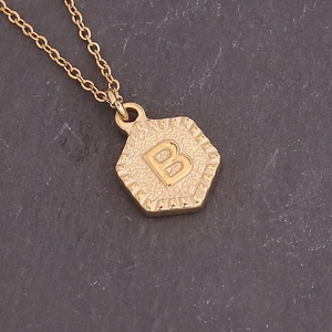 Close-up of golden hexagonal pendant featuring relief letter B on a vintage link chain