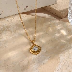 Detailed macro of gold twisted chain and diamond-shaped zircon pendant on stone