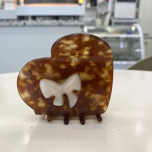 Macro detail of heart-shaped acetate claw clip with amber tortoise pattern and bow