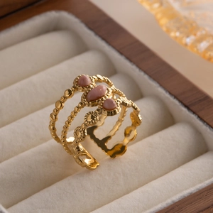 Detail of gold layered wave ring with three pink oval stones on white velvet
