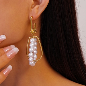 Detailed close-up of geometric gold drop earrings with white pearls on a model
