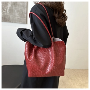Detail of red tote bag with woven texture worn over the shoulder by a model