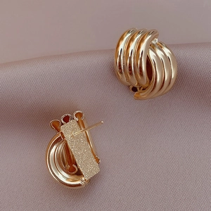 Minimalist geometric overlapping gold stud earrings on premium pink silk background