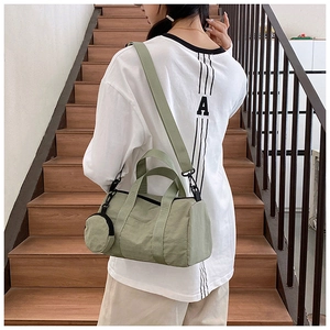 Model wearing a light green nylon barrel fitness bag on stairs showing crossbody style