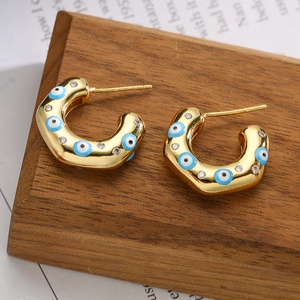 Detailed shot of golden C-shaped hoop earrings with blue evil eye enamel and zircons