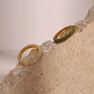 Detailed shot of two gold rings with white and green zircons placed on a textured rock