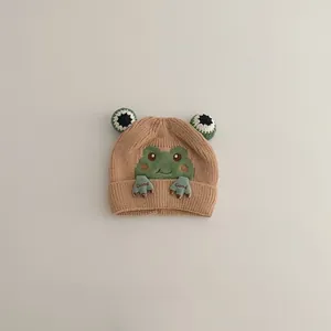 Detailed close-up of beige knitted baby hat with cute green frog embroidery and soft 3D eyes