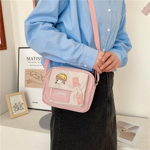 Detail of pink and beige canvas crossbody bag with cartoon pins and adjustable strap