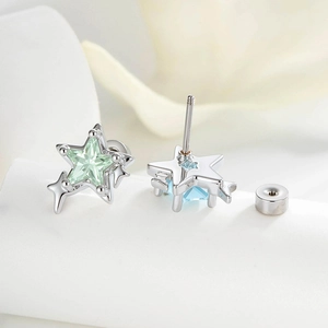 Star-shaped zircon ear studs with green and blue gems on soft white petal background