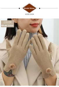 Close-up of khaki winter gloves with plush pom-pom detail worn with a wool coat