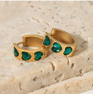 Close-up of 18K gold plated earrings featuring green heart-shaped zircon on marble