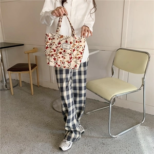Detail of corduroy tote bag with red floral pattern and square label in a cafe setting