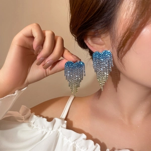 Close-up of heart tassel earrings with blue and yellow gradient rhinestones on model