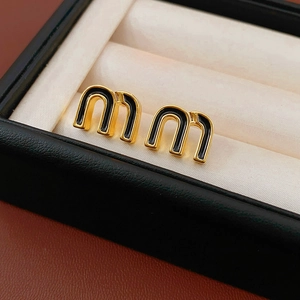 Macro shot of gold-plated M-letter stud earrings with black enamel inlay detail