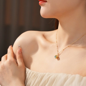 Detail of gold-plated cube pendant necklace with blue and yellow cat-eye stones