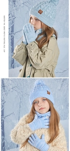 Detail of light blue cable knit kids set including pompom hat, scarf and gloves in snow