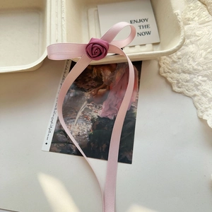 Detailed close-up of a pink ribbon bow hair tie with a purple rose on a vintage tray