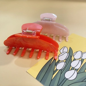 Detail of pink and orange acrylic shark hair clips with subtle glitter on a beige background