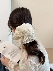 Detailed view of a cream lace bow scrunchie styled on a low ponytail hair tie