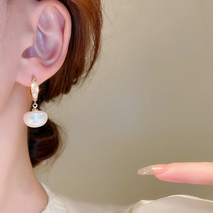 Gros plan de boucles d'oreilles huggies dorées avec diamants pavés et gouttes de perles