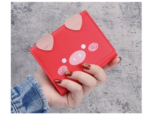 Close-up of red cartoon pig wallet with pink heart details held by a person