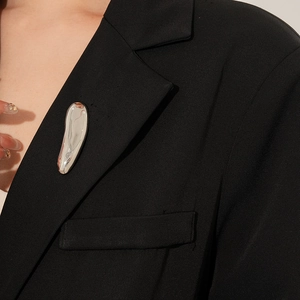 Polished silver liquid metal brooch pinned on a black suit lapel close-up view