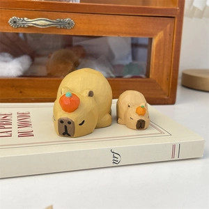 Close-up of two handcrafted wooden capybara figurines with orange accents on a book