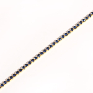 Detailed diagonal shot of a gold tennis bracelet featuring round-cut blue cubic zirconia