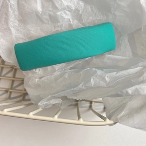 Detail shot of a turquoise fabric-covered rectangular hair clip on soft white paper