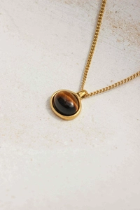 Macro shot of 18K gold chain with oval tiger eye stone pendant on light texture background