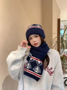 Dettaglio del set cappello e sciarpa in maglia blu scuro con motivi a fiocchi di neve rossi