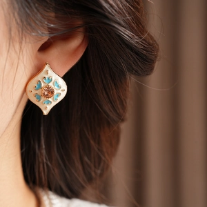 Close-up of vintage gold-framed diamond-shaped earrings with enamel patterns and gemstones