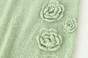 Macro view of mint green knit dress showing 3D floral embroidery and textured fabric