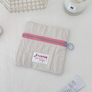 Detail of beige pleated fabric pouch featuring contrast pink zipper and blue ring pull
