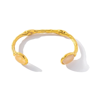 Detail of gold bark texture cuff bracelet with two pink oval stones on white background