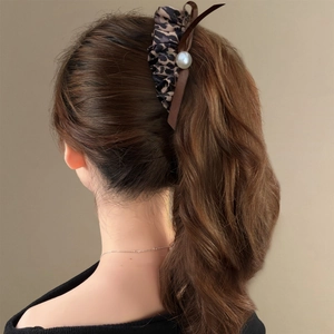 Detailed view of leopard print bow hair clip with large pearl and brown ribbon on hair