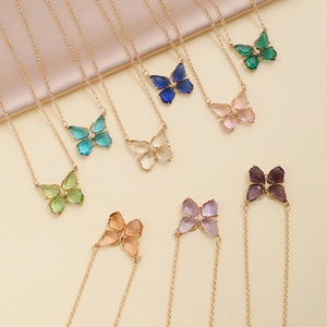Colorful zircon butterfly necklaces with gold chains on beige fabric background