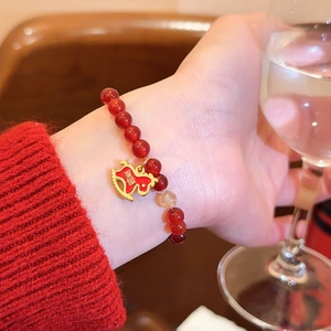 Detailansicht eines Armbands aus roten Achatperlen mit goldenem Schaukelpferd-Anhänger.