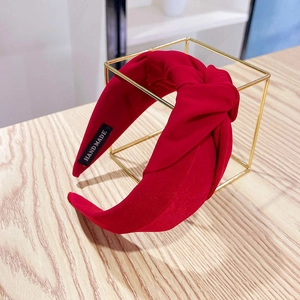Close-up of deep red knotted fabric headband showing the handmade label on the inner side