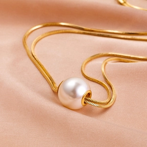 Detail of a gold snake chain necklace with a round white pearl on champagne silk fabric