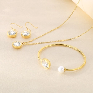 Detailed view of gold jewelry set with round clear gems and pearls on beige silk fabric