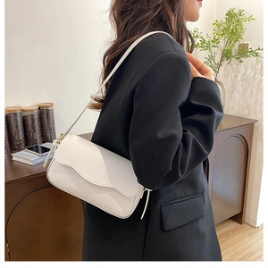 Detail view of the white leather shoulder bag with flap design worn by a model