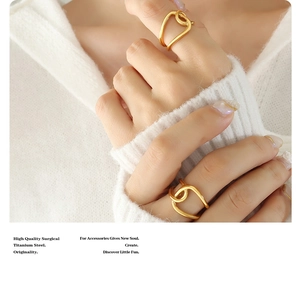 Detail of twisted geometric gold titanium steel rings worn over white knitwear fabric
