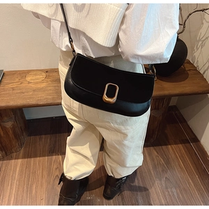 Black leather saddle bag featuring a gold rectangular buckle shown on a model's shoulder