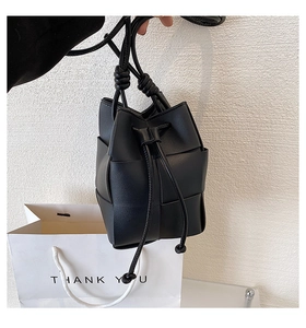 Detail of black woven bucket bag with drawstring closure and knotted leather strap