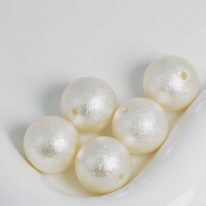 Close-up of five white wrinkled faux pearl round beads with holes in a ceramic dish