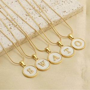 Detail view of five 18K gold snake chains with white shell alphabet initial pendants