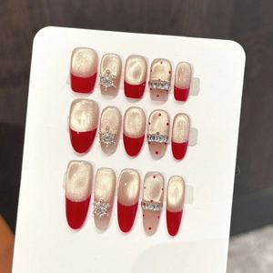 Close-up of red and champagne gold press-on nails with rhinestones and snowflakes