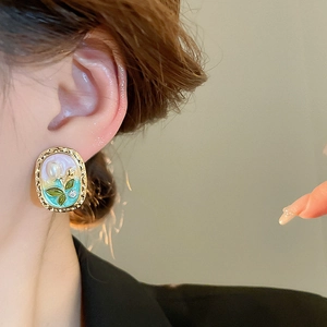 Vintage oval enamel earrings with blue floral patterns and pearls worn by a model